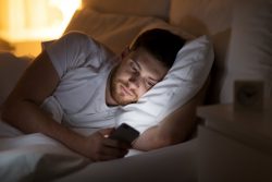 Man lying in bed, experiencing negative effects of cell phones and sleep apnea