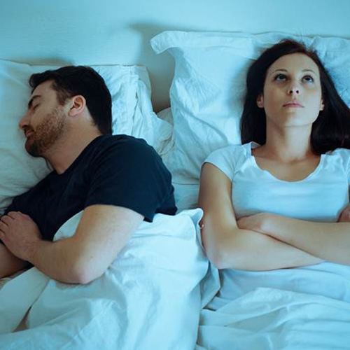 Couple in bed, husband is snoring and wife is annoyed