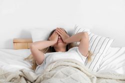 Woman in bed, covering her eyes