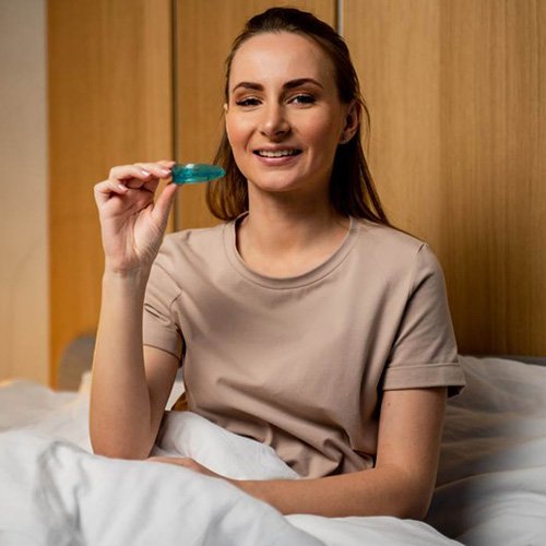 Woman sitting up in bed, holding her oral sleep appliance