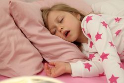 Snoring little girl on pink bed sheets