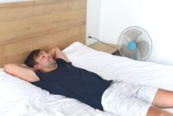 Man sleeping next to fan during hot summer weather