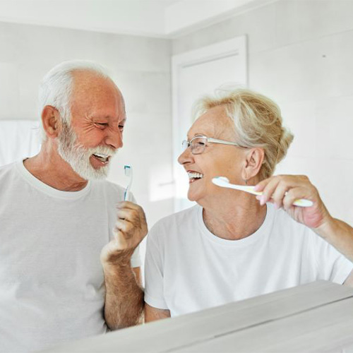 Older couple brushing their teeth in front of bathroom mirror